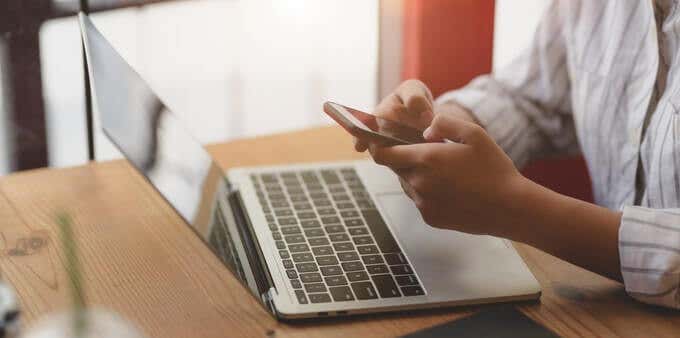 Someone sitting at a laptop holding an iPhone 